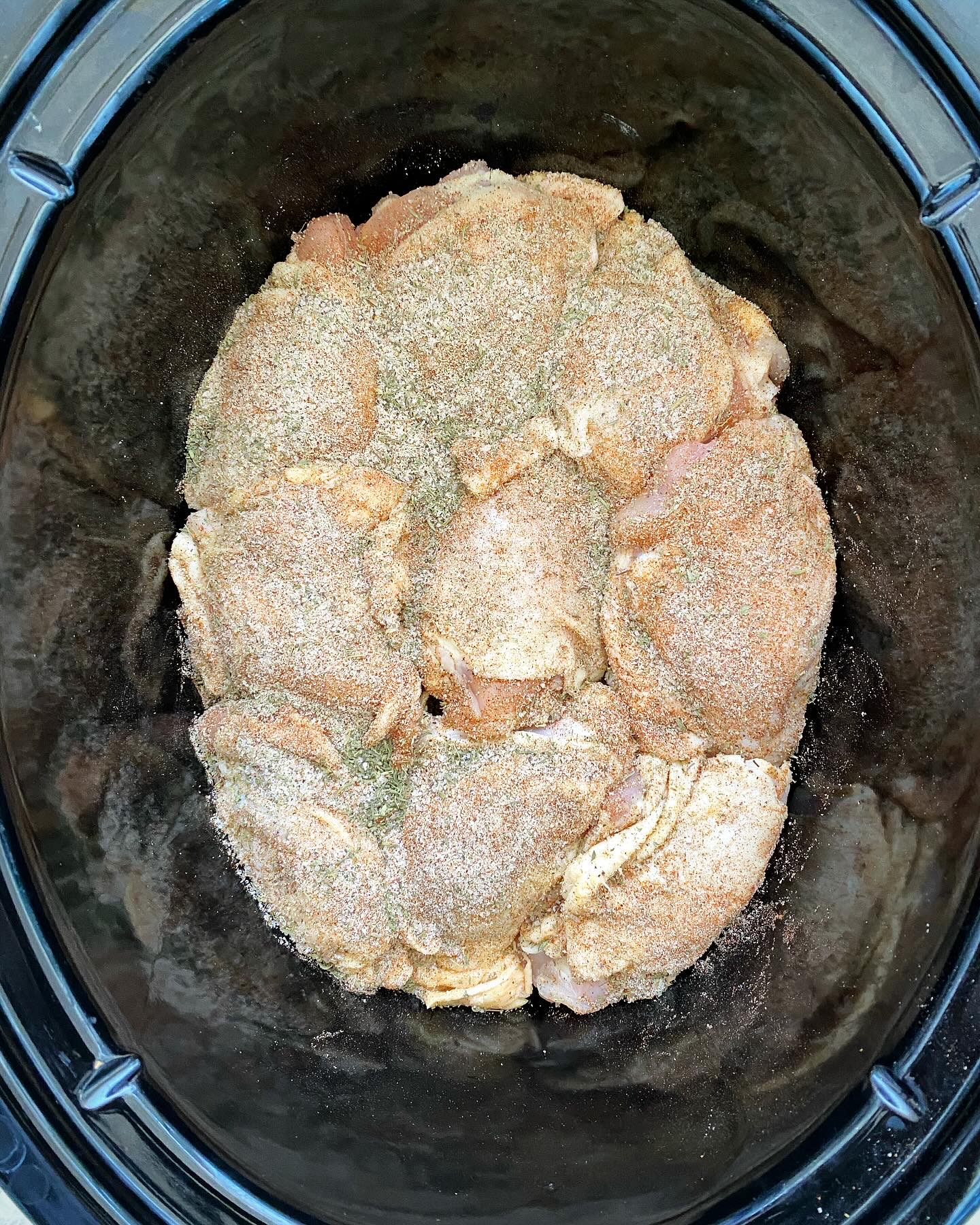 overhead shot of uncooked bone-in, skin-on chicken thighs in a black slow cooker
