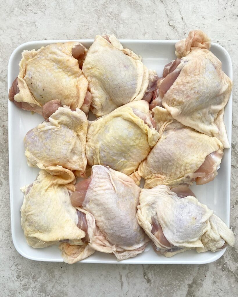 raw skin-on, bone-in chicken thigs on a white platter