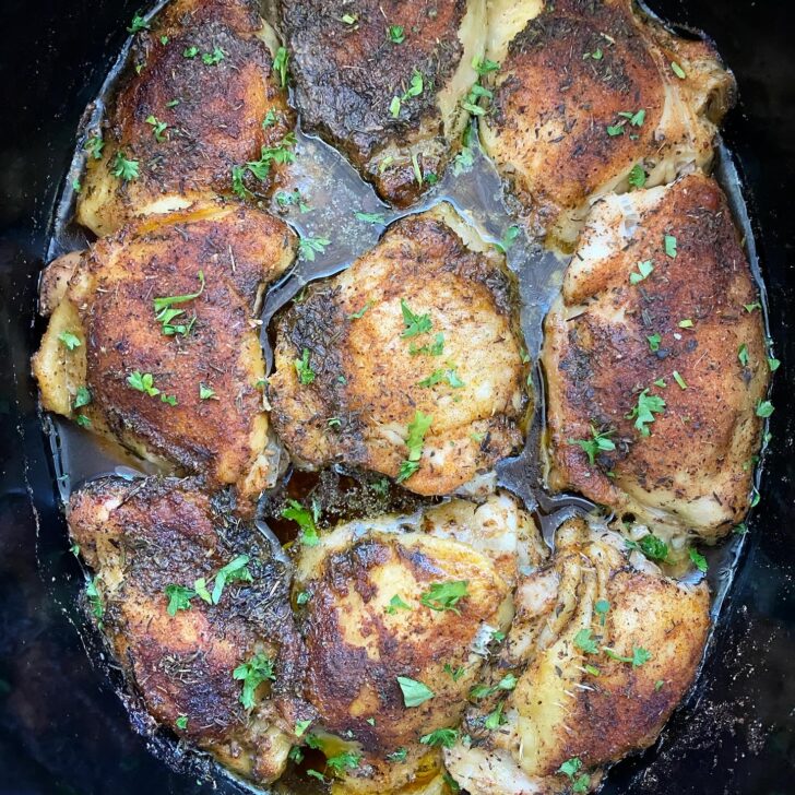 overhead shot of cooked bone-in, skin-on chicken thighs in a black slow cooker garnished with fresh parsley