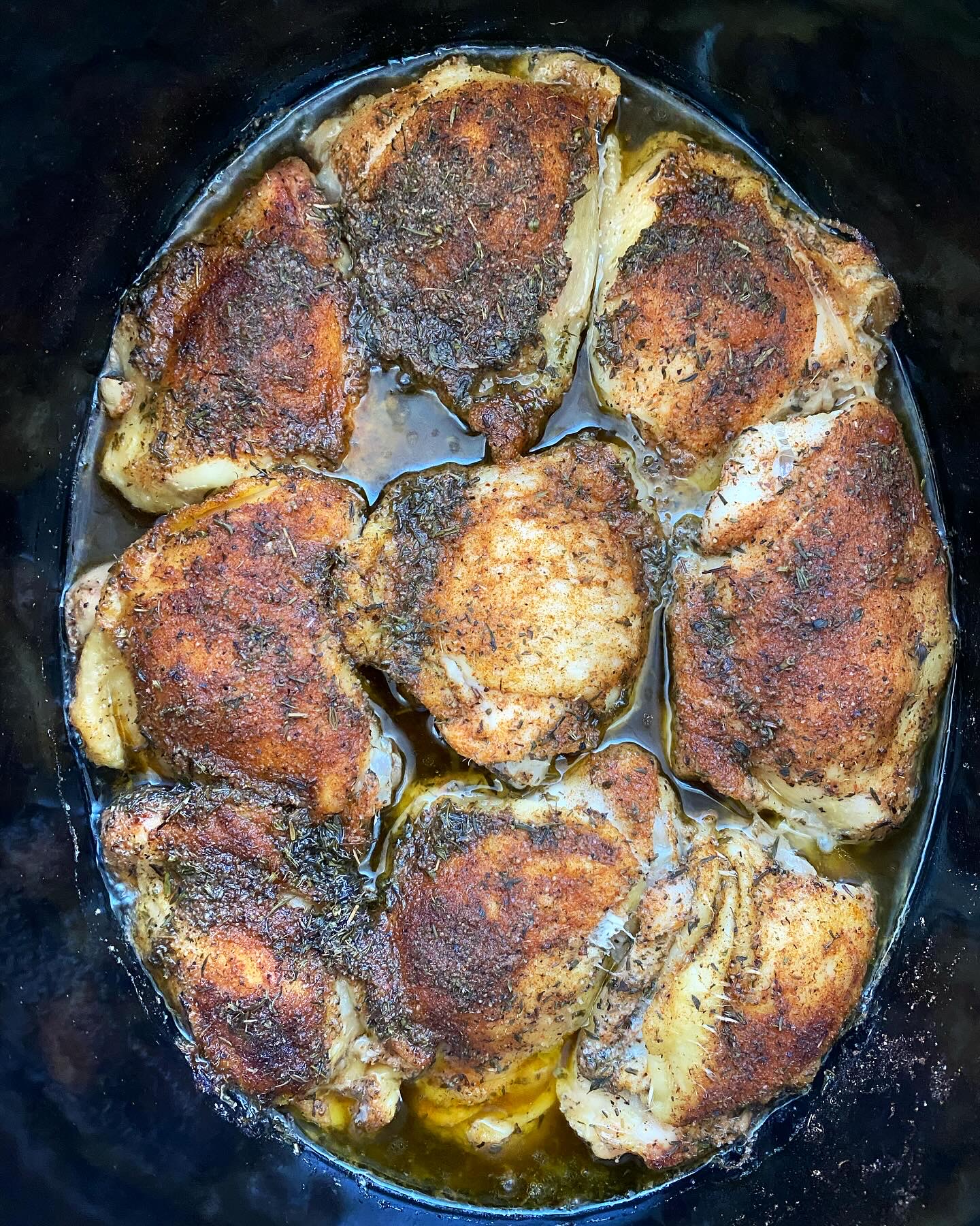 overhead shot of cooked bone-in, skin-on chicken thighs in a black slow cooker
