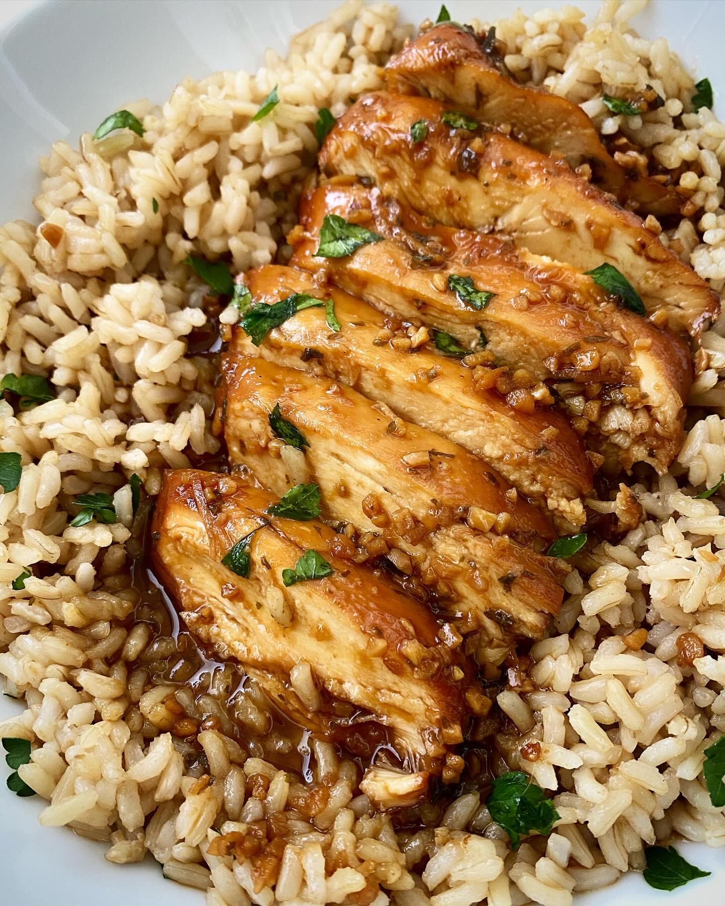 close up shot of cooked honey garlic chicken in a white bowl on top of brown rice