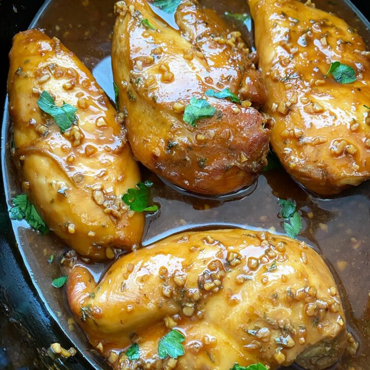 close up shot of cooked honey garlic chicken in a black slow cooker garnished with fresh parsley