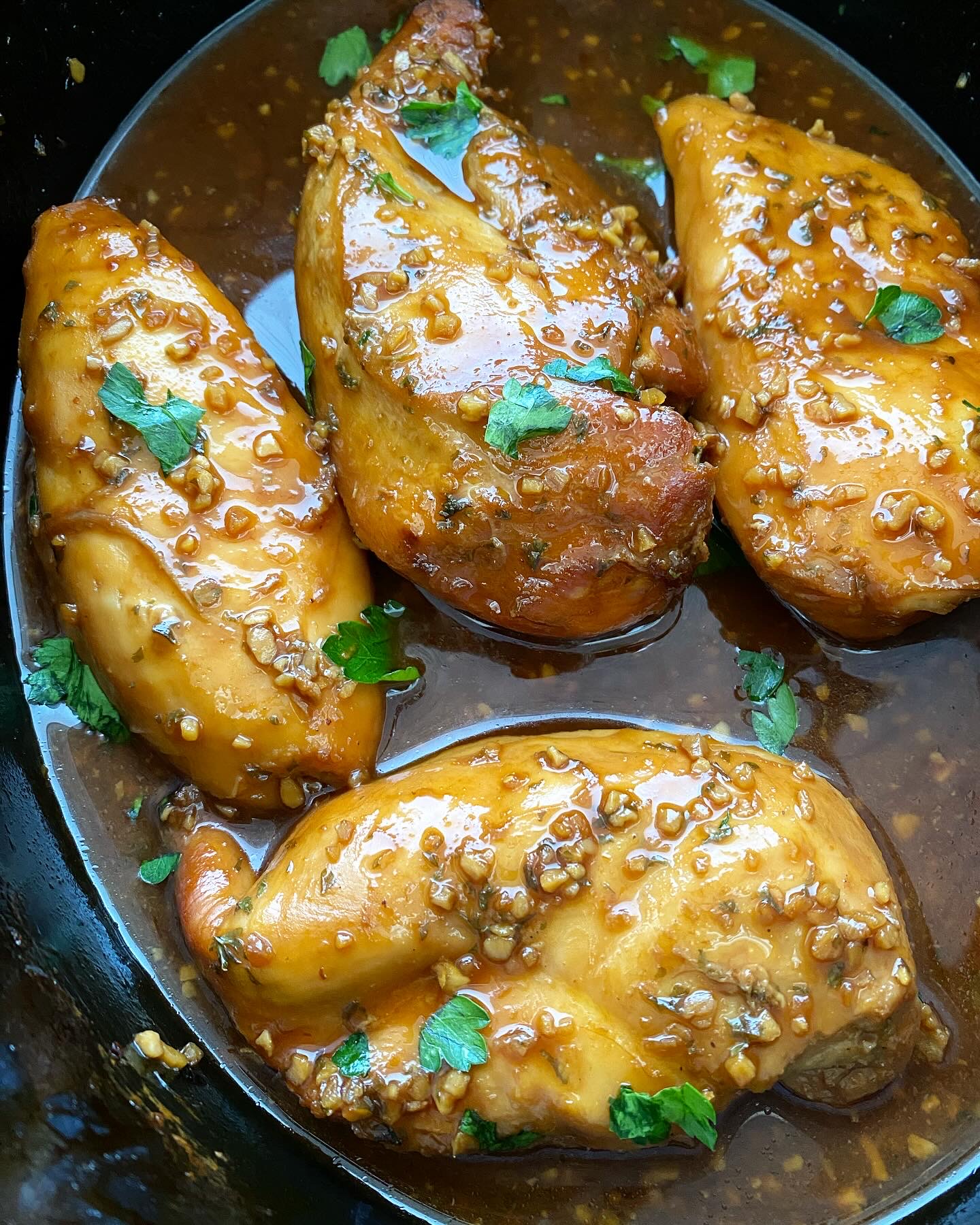 close up shot of cooked honey garlic chicken in a black slow cooker garnished with fresh parsley