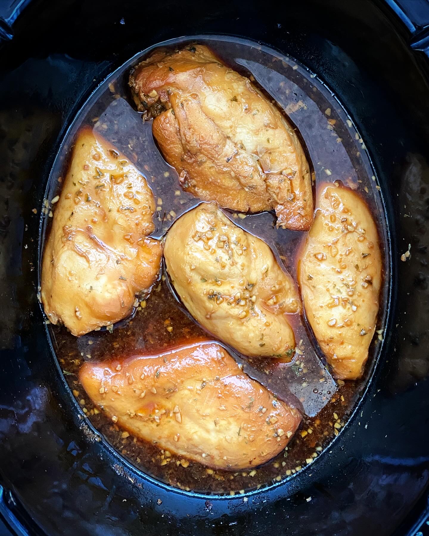 overhead shot of cooked honey garlic chicken in a black slow cooker
