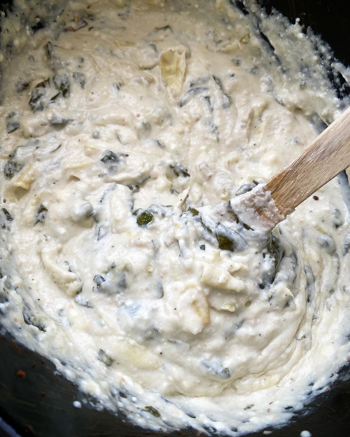 close up shot of cooked Crockpot Spinach Artichoke Dip in a black slow cooker