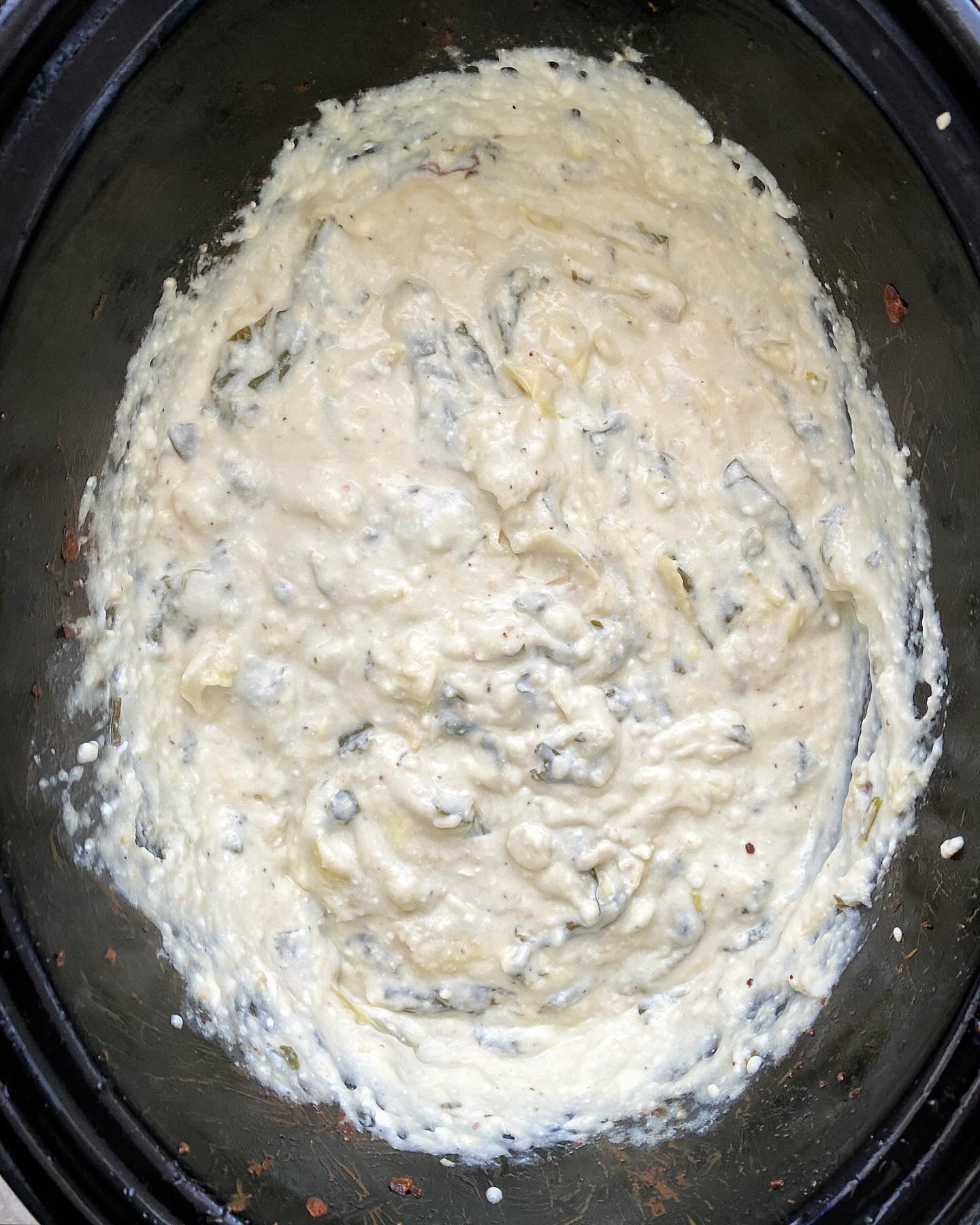 overhead shot of cooked Crockpot Spinach Artichoke Dip in a black slow cooker