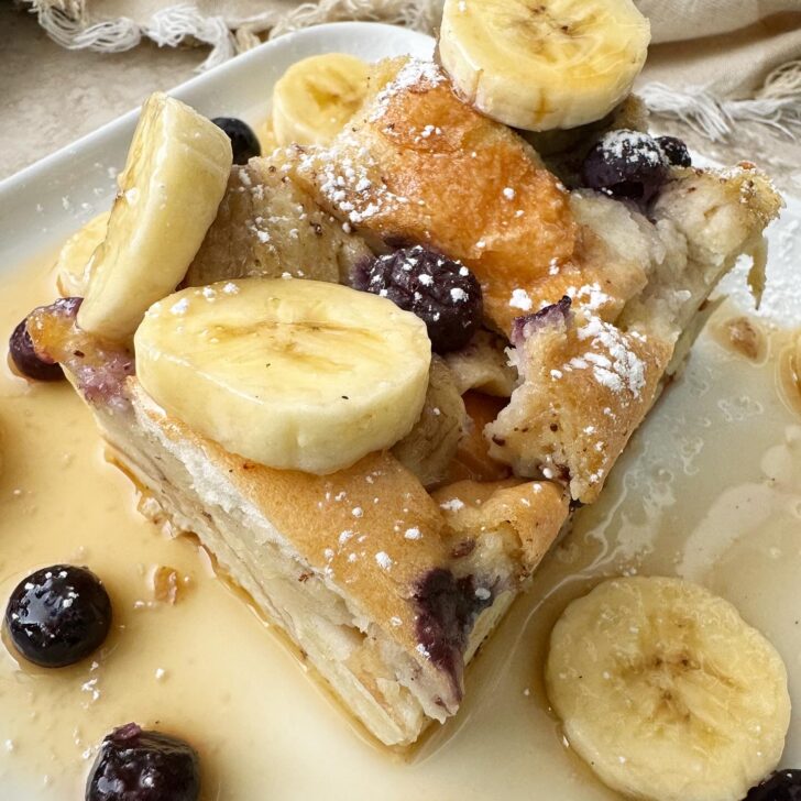 close up shot of sliced banana blueberry french toast on a white plate garnished with powdered sugar and syrup