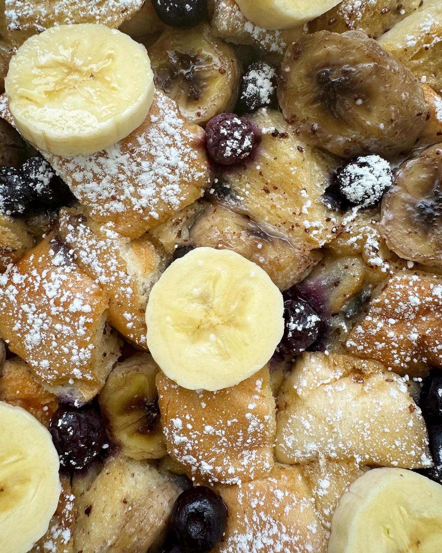 close up shot of banana blueberry french toast on a white plate garnished with powdered sugar