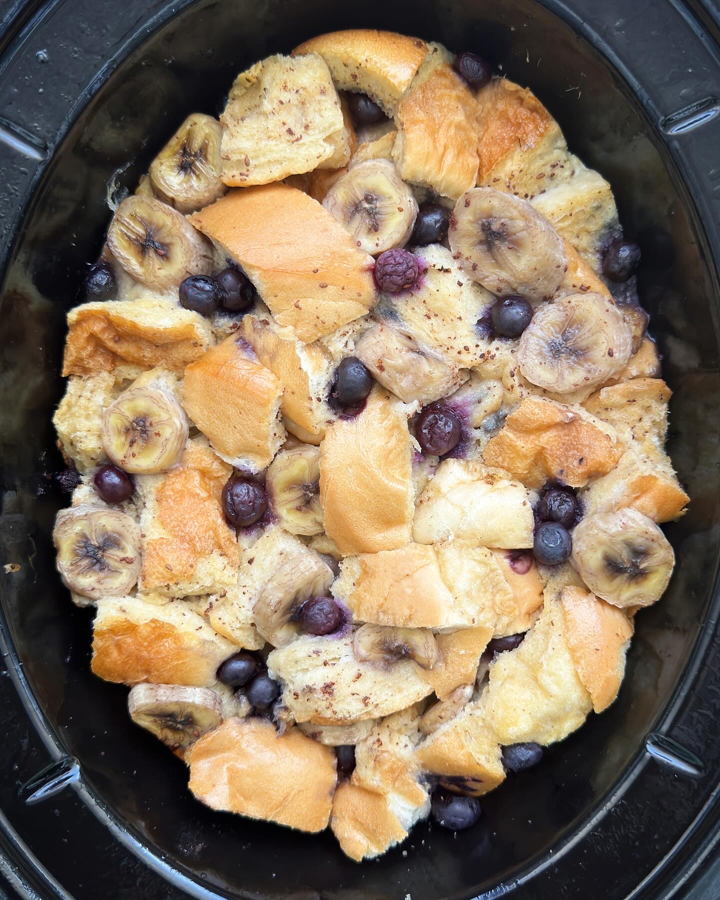 overhead shot of cooked banana blueberry french toast in a black slow cooker