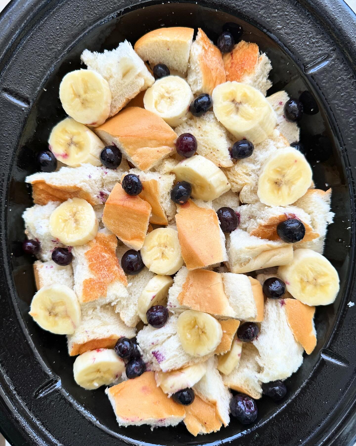 overhead shot of uncooked banana blueberry french toast in a black slow cooker