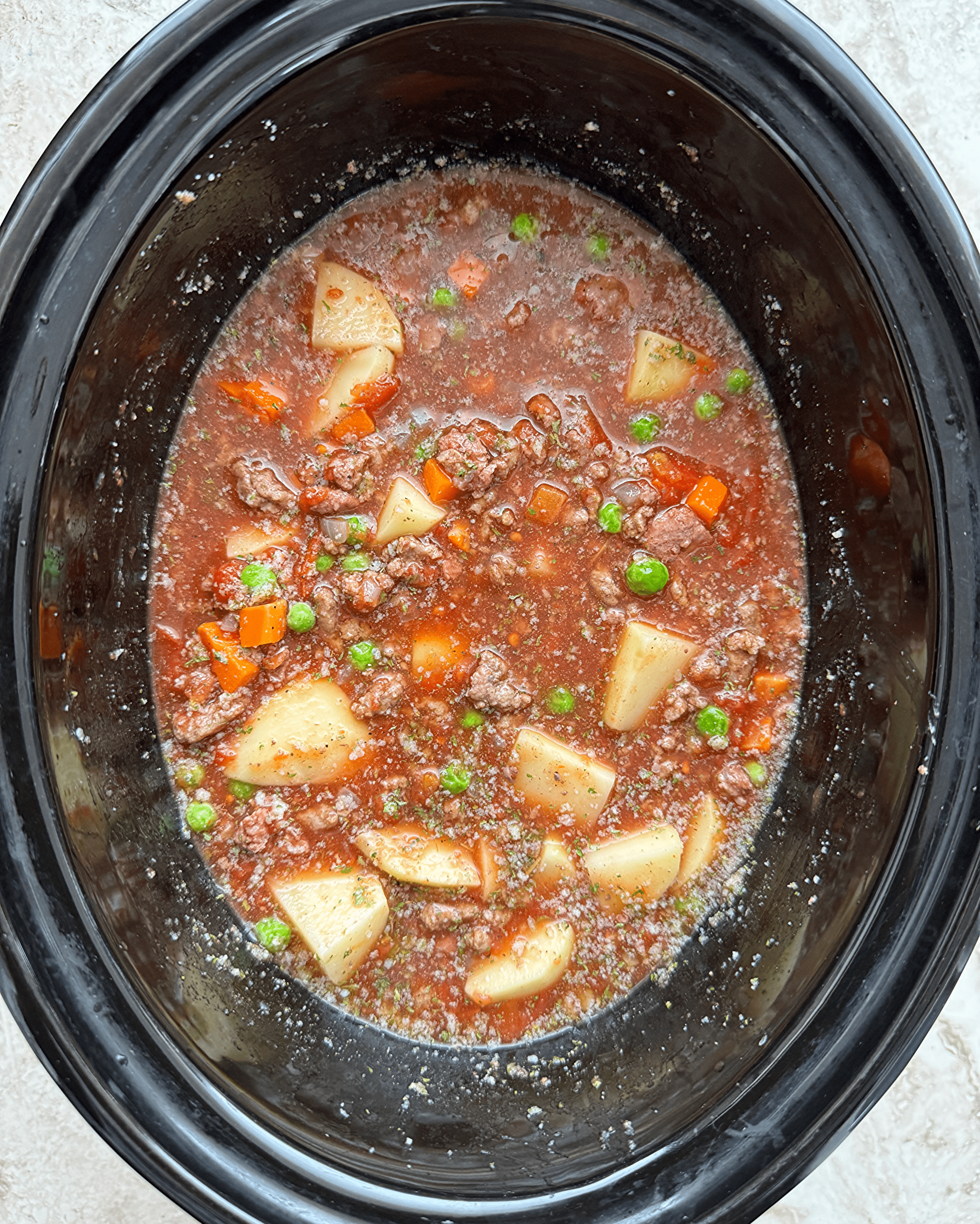 overhead shot of uncooked poor man's stew in a black slow cooker