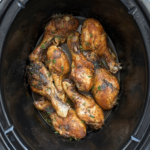 overhead shot of cooked chicken legs in a black slow cooker