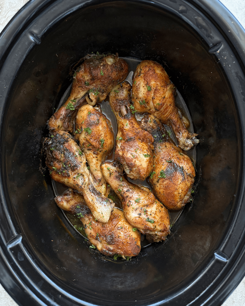overhead shot of cooked chicken legs in a black slow cooker