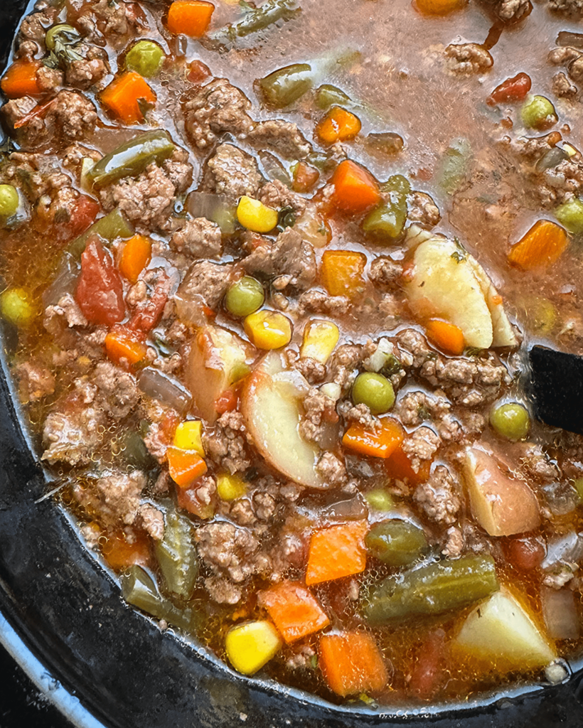 close up shot of crockpot ground beef vegetable soup in a black slow cooker