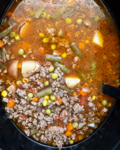 overhead shot of cooked crockpot ground beef vegetable soup in a black slow cooker