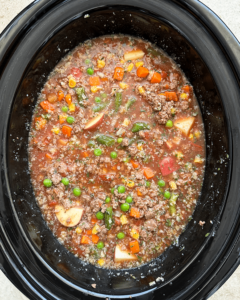 overhead shot of uncooked crockpot ground beef vegetable soup in a black slow cooker