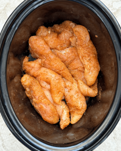 overhead shot of uncooked BBQ chicken tenders in a black slow cooker