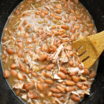 overhead shot of cooked Slow Cooker Southern Pinto Beans with smoked turkey in a black slow cooker with a wooden spoon