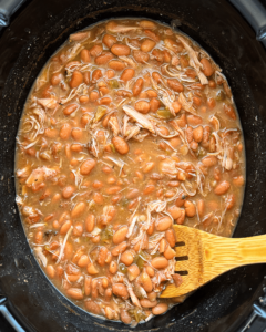 overhead shot of cooked Slow Cooker Southern Pinto Beans with smoked turkey in a black slow cooker with a wooden spoon