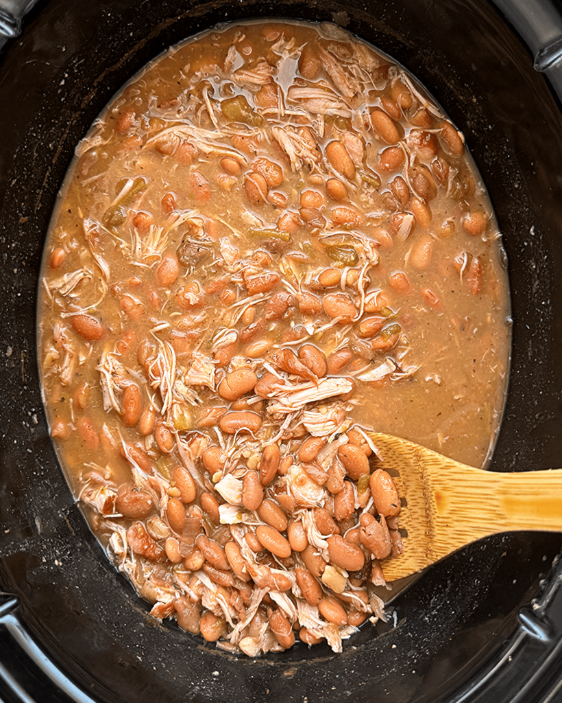 overhead shot of cooked Slow Cooker Southern Pinto Beans with smoked turkey in a black slow cooker with a wooden spoon