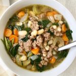 overhead shot of beef bean spinach soup in a white bowl with a silver spoon
