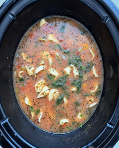 overhead shot of cooked vegetable tortellini soup in a black slow cooker