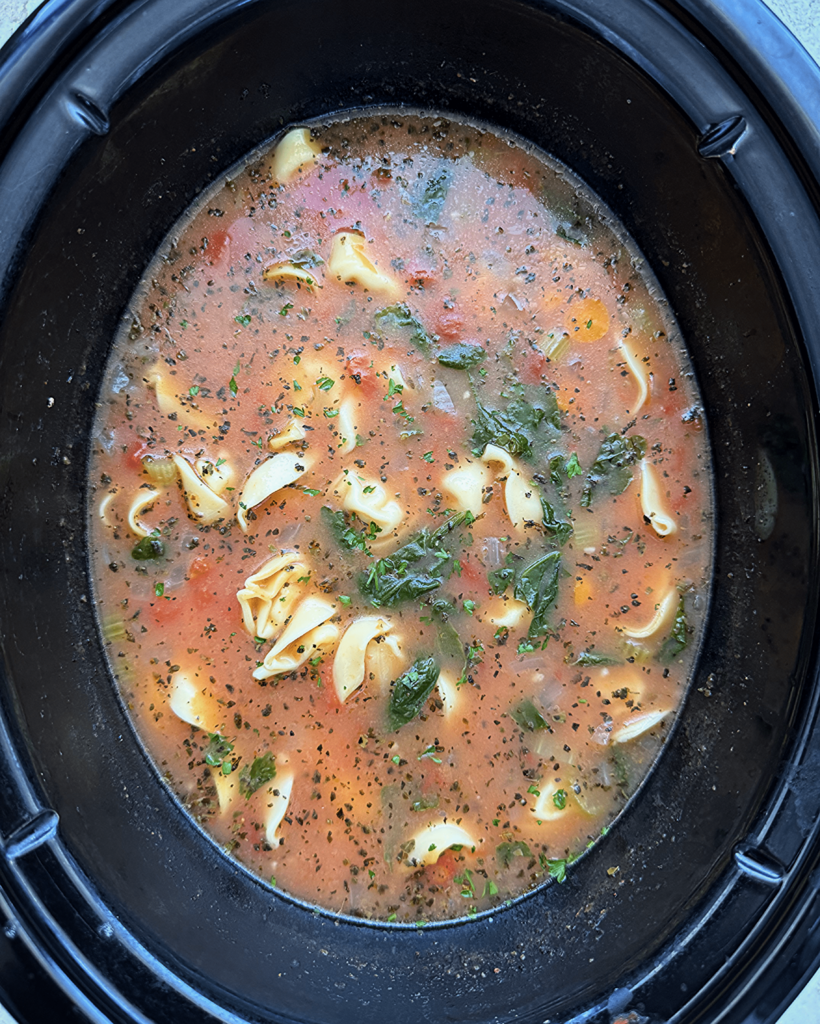 overhead shot of cooked vegetable tortellini soup in a black slow cooker