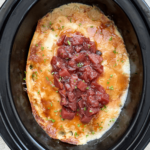 overhead shot of cooked Crockpot Leftover Thanksgiving Casserole in a black slow cooker garnished with fresh cranberry sauce