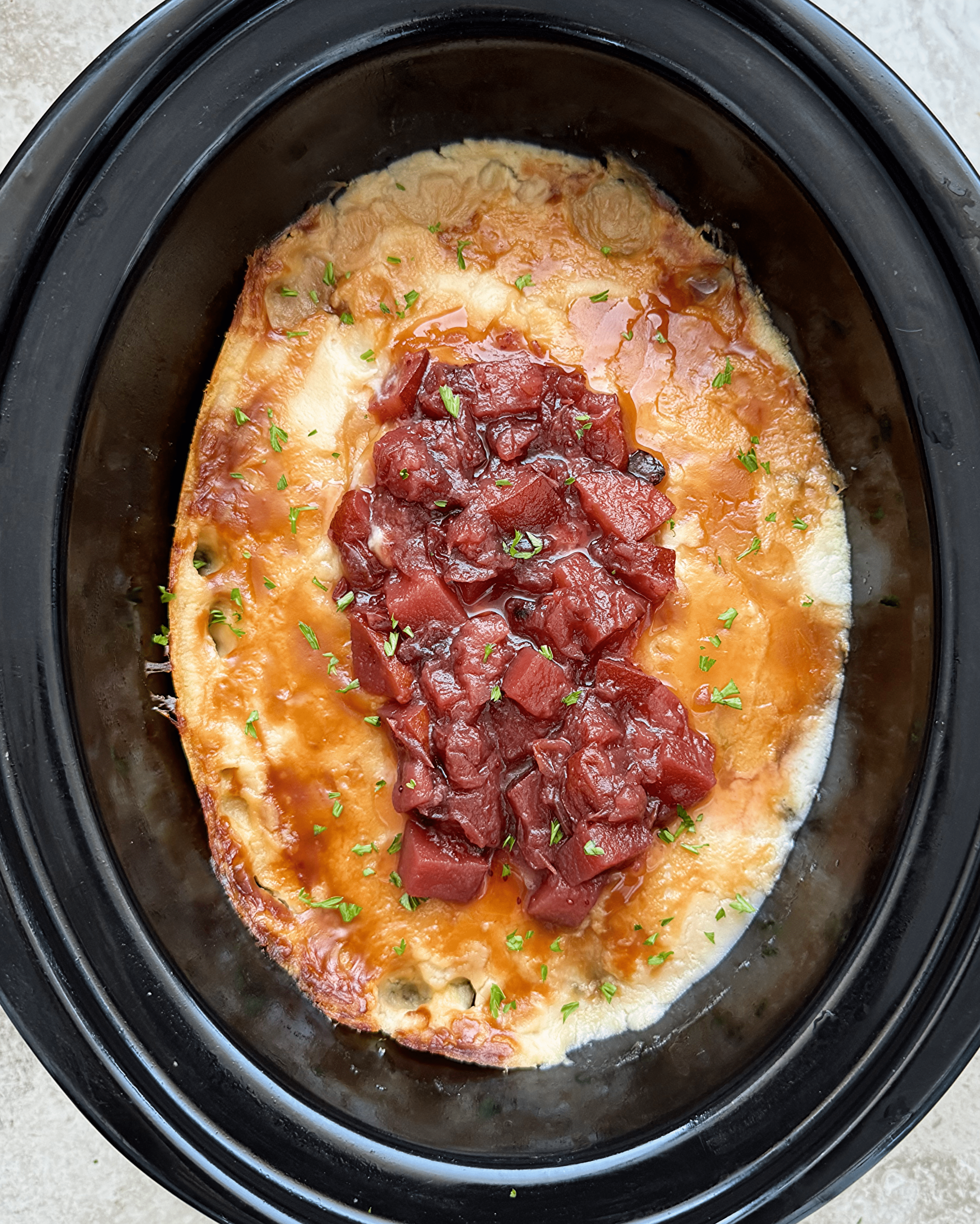 overhead shot of cooked Crockpot Leftover Thanksgiving Casserole in a black slow cooker garnished with fresh cranberry sauce
