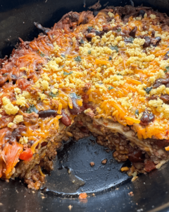 overhead shot of cooked chili casserole in a black slow cooker with a piece missing