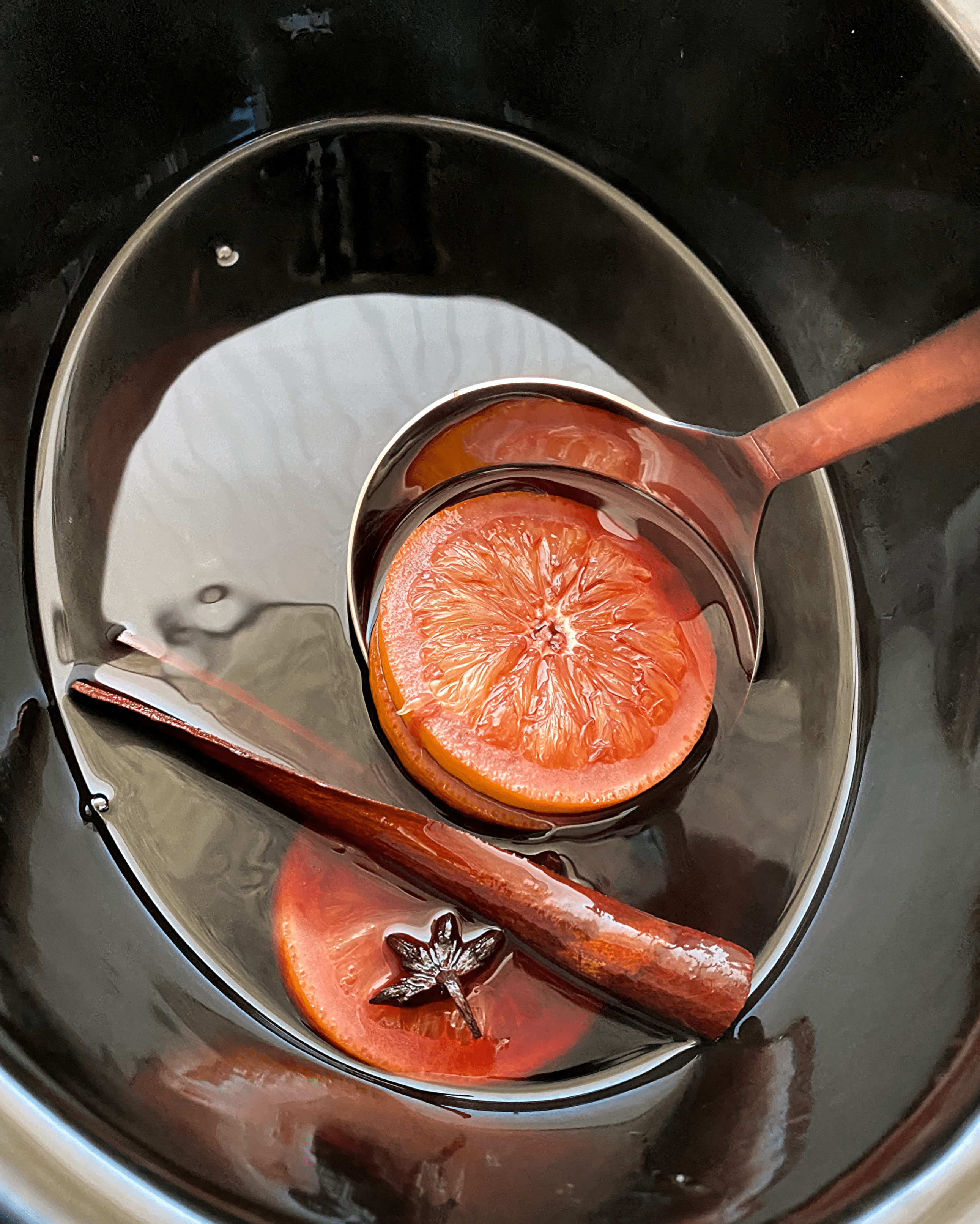 overhead shot of cooked mulled wine in a black slow cooker