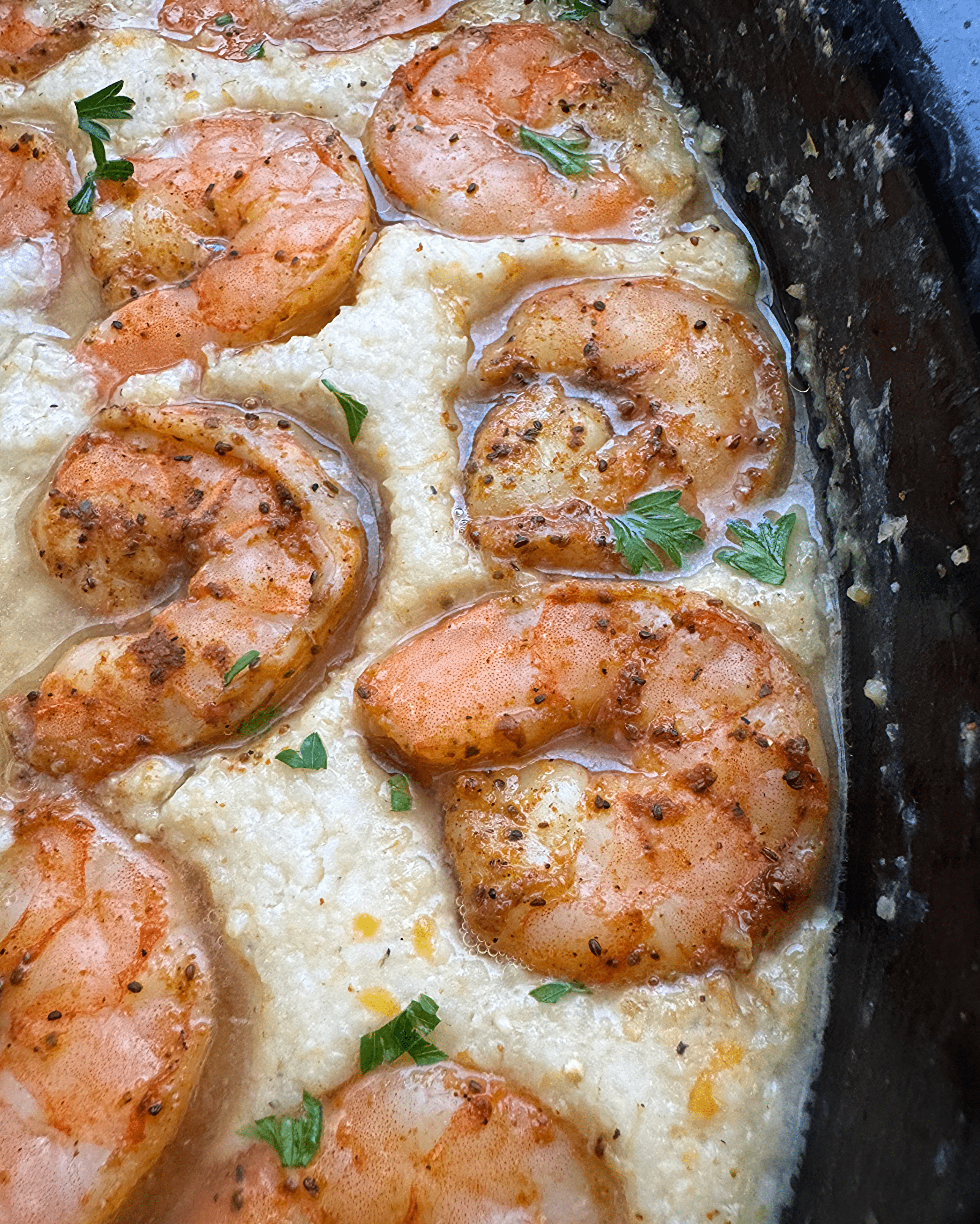 close up shot of cooked shrimp and grits in a black slow cooker garnished with fresh parsley