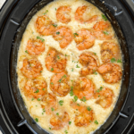 overhead shot of cooked grits with cooked shrimp in a black slow cooker garnished with fresh parsley