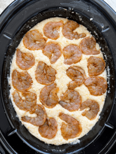 overhead shot of cooked grits with uncooked shrimp in a black slow cooker