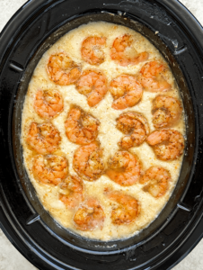 overhead shot of cooked grits with cooked shrimp in a black slow cooker