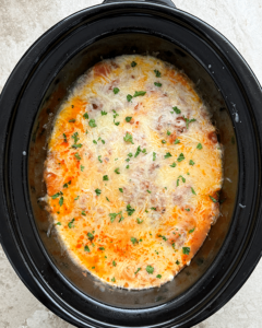 overhead shot of cooked ravioli casserole in a black slow cooker with melted cheese on top