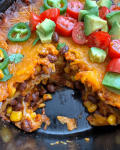 overhead shot of cooked slow cooker vegetarian enchilada casserole in a black slow cooker with a piece missing