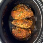 overhead shot of cooked Bone-In Chicken Breasts in a black slow cooker garnished with fresh parsley