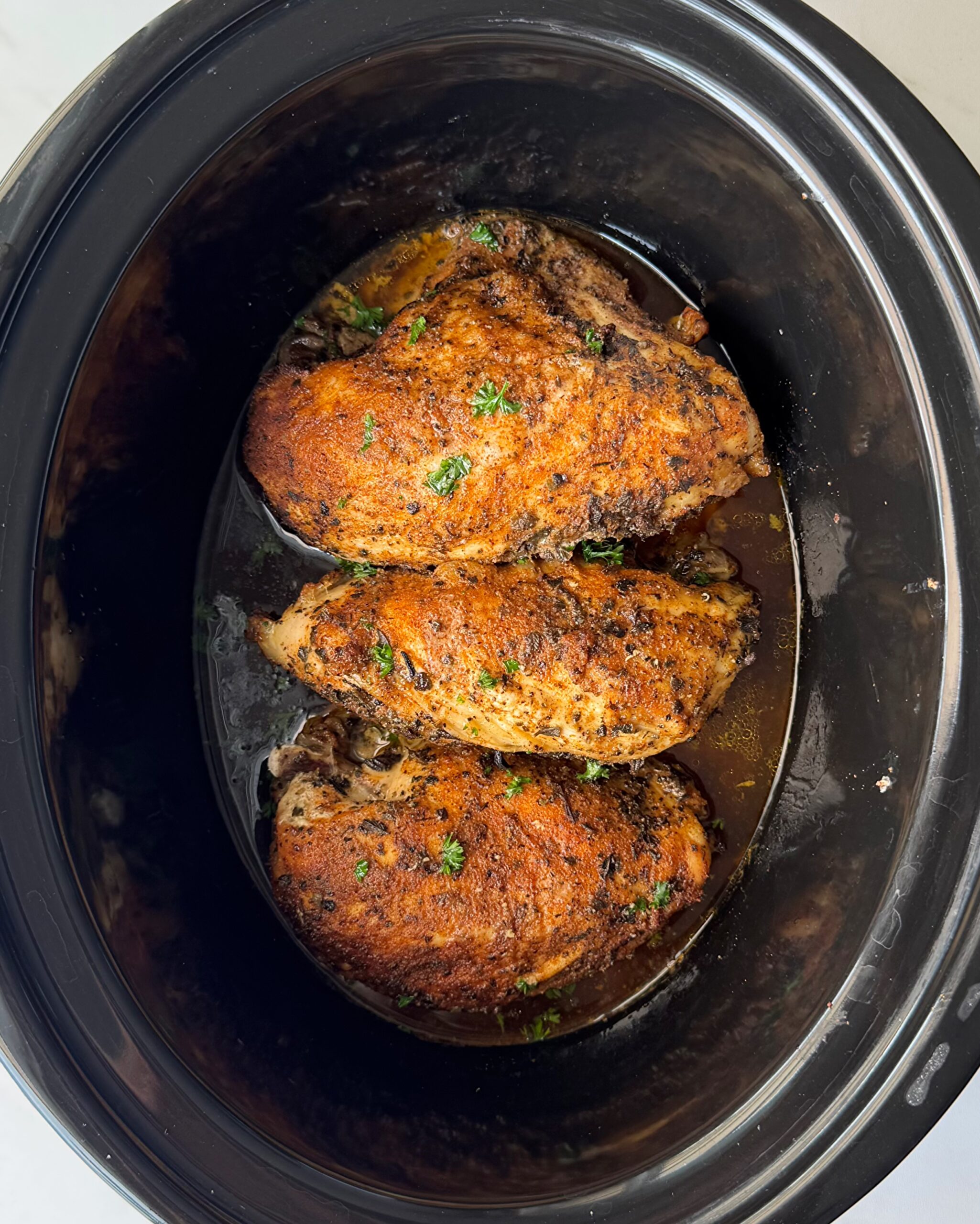 overhead shot of cooked Bone-In Chicken Breasts in a black slow cooker garnished with fresh parsley
