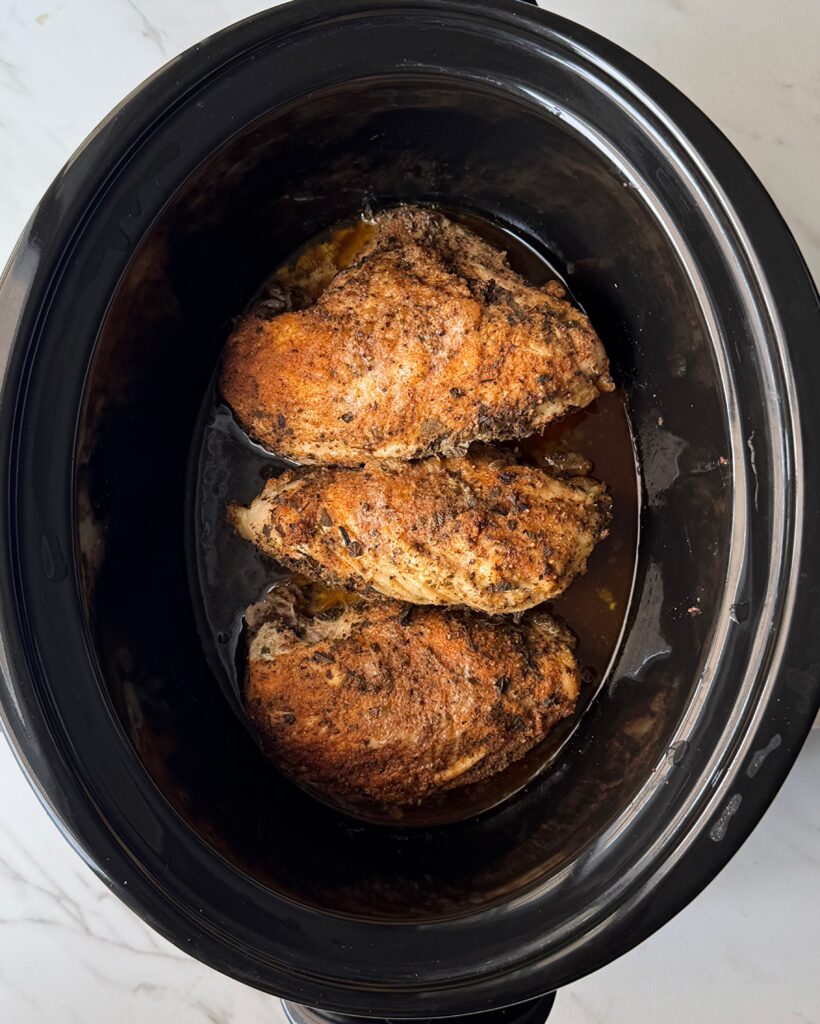 overhead shot of cooked Bone-In Chicken Breasts in a black slow cooker