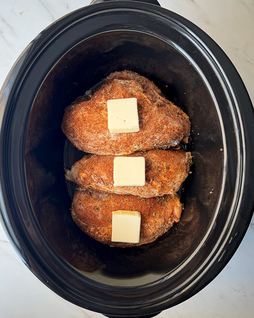 overhead shot of uncooked Bone-In Chicken Breasts in a black slow cooker