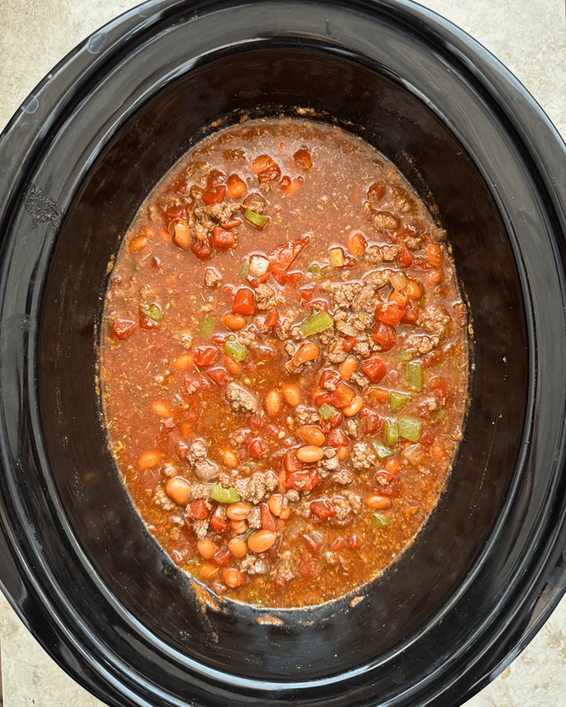 overhead shot of uncooked Chili Mac And Cheese in a black slow cooker