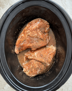 overhead shot of uncooked slow cooker bone in chicken breasts in a black slow cooker