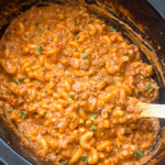 overhead shot of Homemade Hamburger Helper in a black slow cooker with a wooden spoon