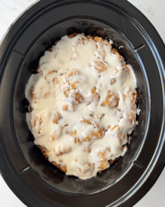 overhead shot of cooked Cinnamon Roll Casserole in a black slow cooker with icing