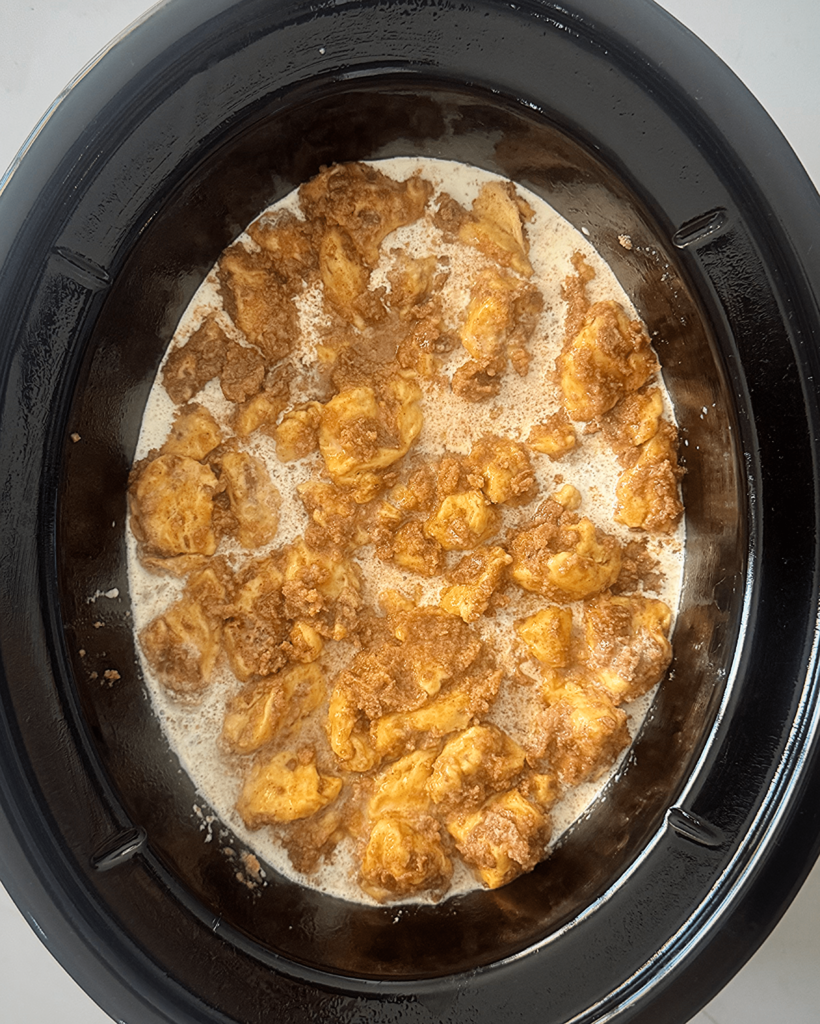 overhead shot of uncooked Cinnamon Roll Casserole in a black slow cooker