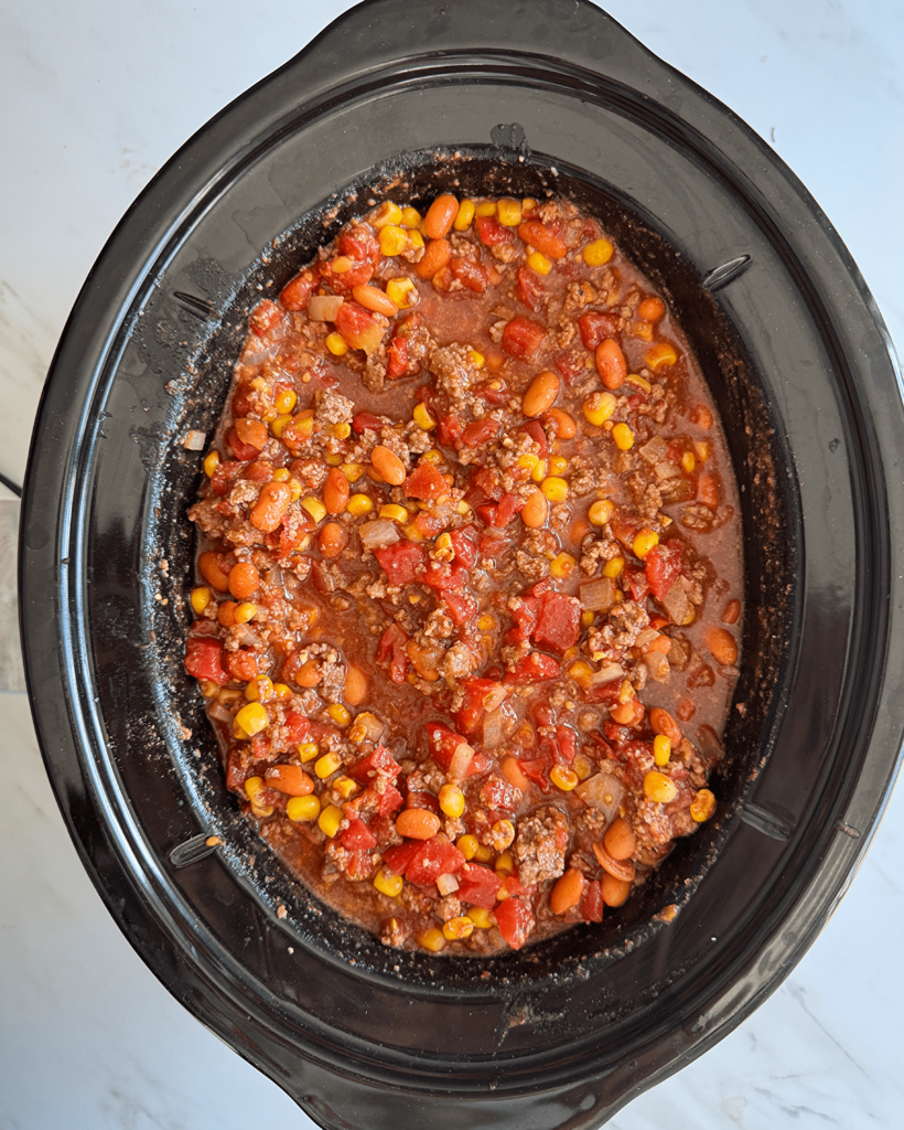 overhead shot of uncooked taco chili in a black slow cooker