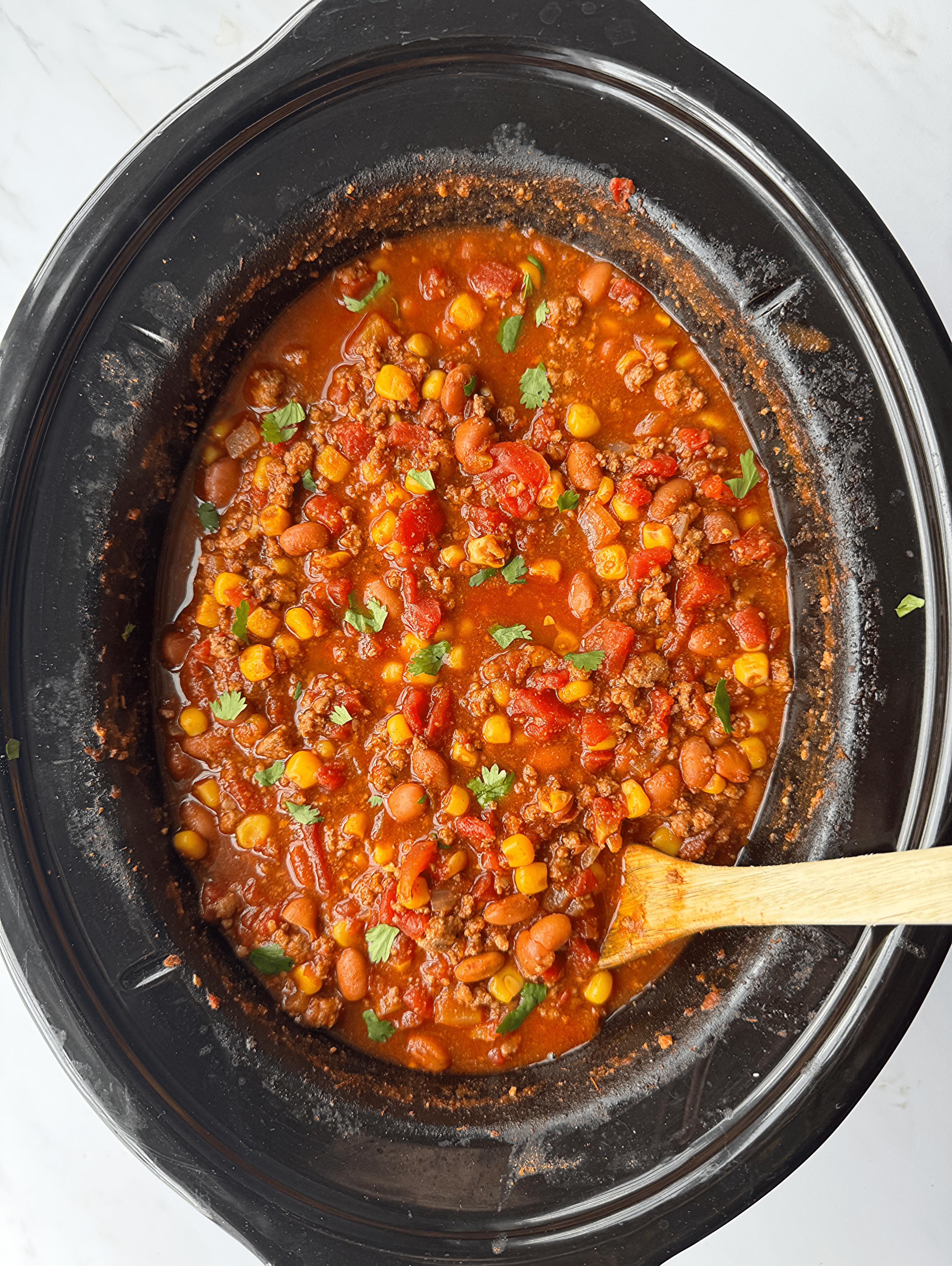 overhead shot of cooked taco chili in a black slow cooker garnished with fresh cilantro