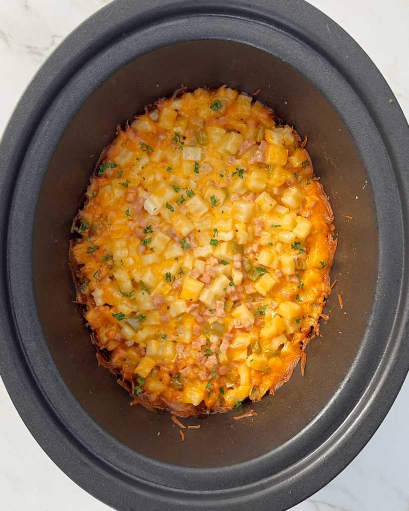 overhead shot of cooked Cheesy Breakfast Potatoes in a black slow cooker