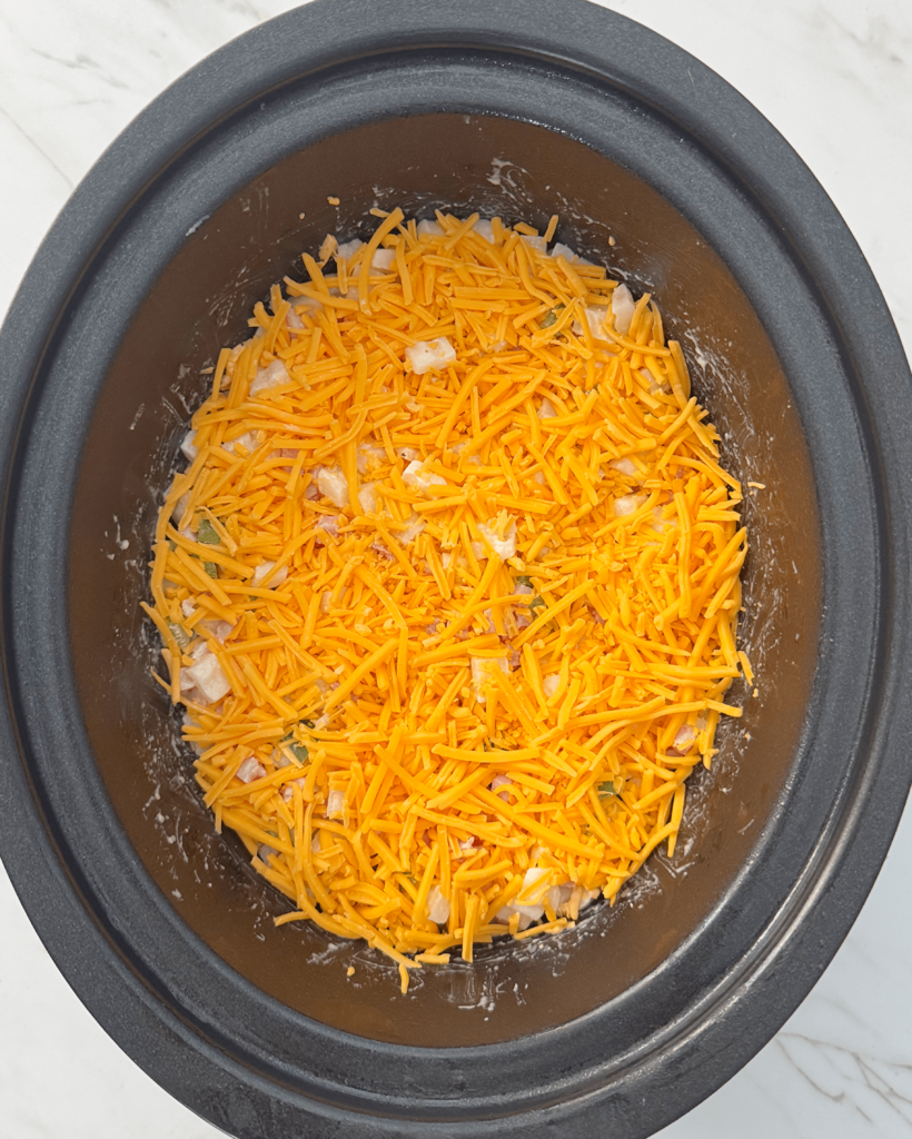 overhead shot of uncooked Cheesy Breakfast Potatoes in a black slow cooker
